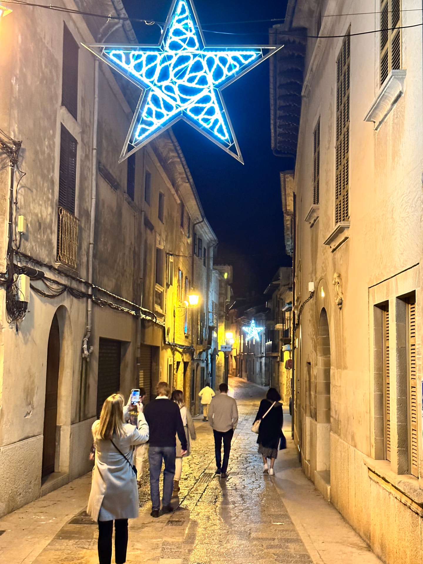Star-shaped Christmas lights over a narrow street in Pollença old town at night