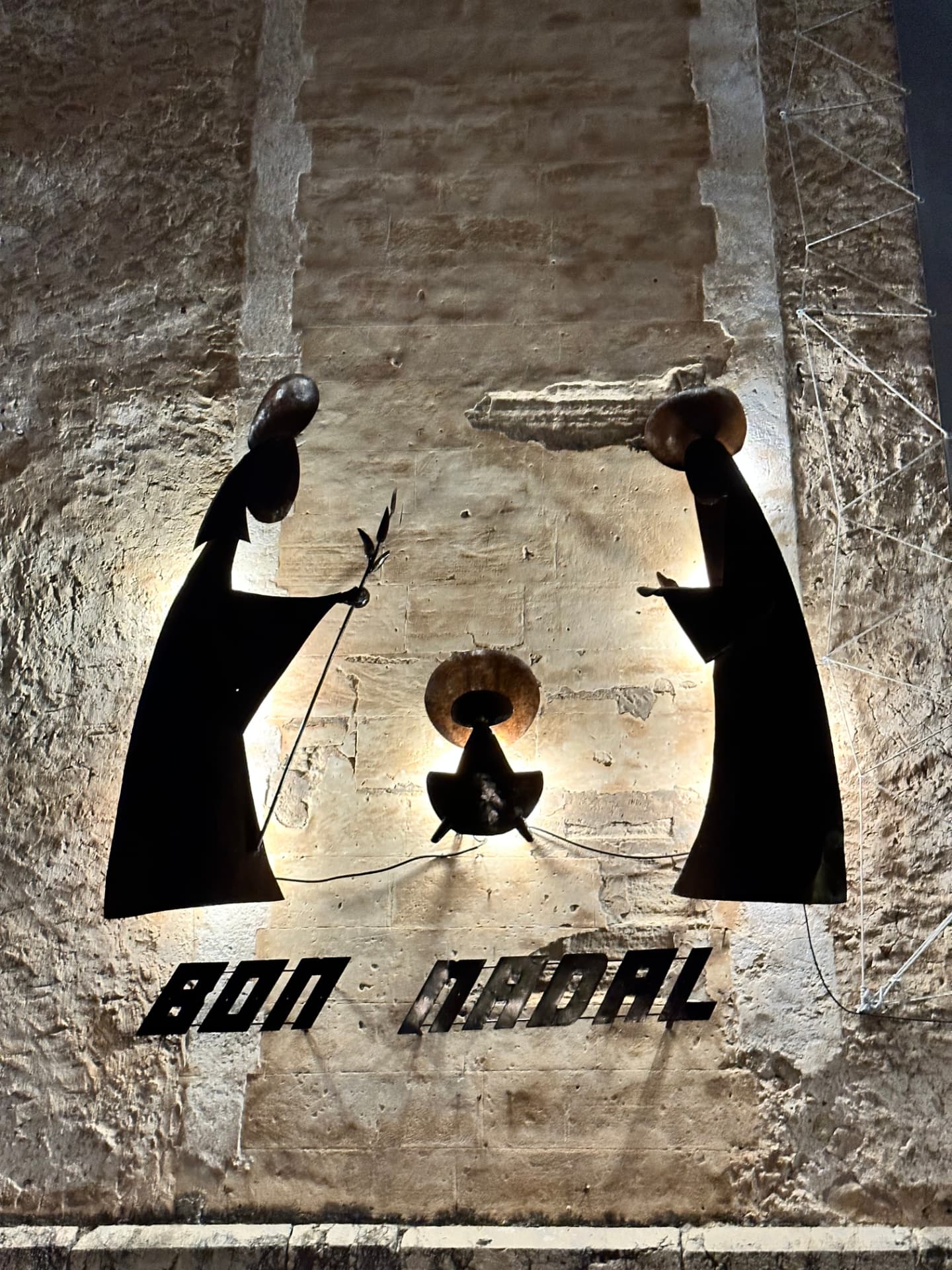 Metal nativity silhouettes and the words Bon Nadal on a stone church wall
