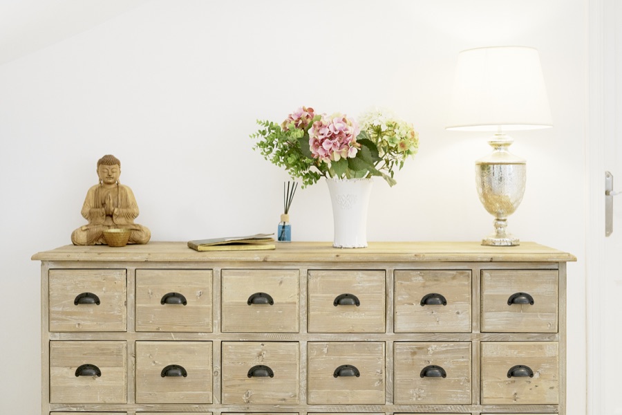 A wooden chest with flowers, lamp and Buddha ornament