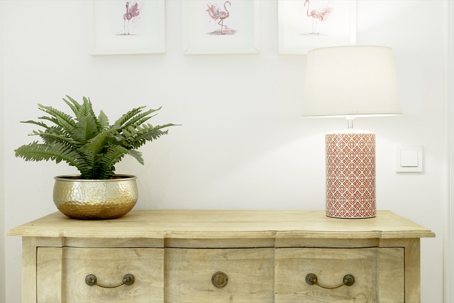 A wooden bedroom chest with plant and decorative lamp